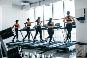 Running on a treadmill. Group of young sportive people have crossfit day indoors in gym photo