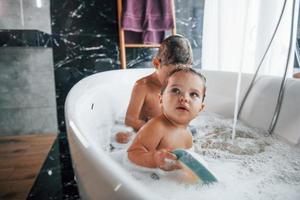 Two kids having fun and washing themselves in the bath at home. Helping each other photo