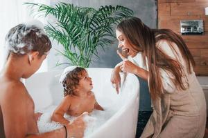 Having fun. Young mother helps her son and daughter. Two kids washing in the bath photo