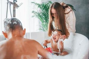 Having fun. Young mother helps her son and daughter. Two kids washing in the bath photo