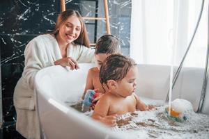 Young mother helps her son and daughter. Two kids washing in the bath photo