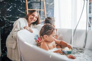 Young mother helps her son and daughter. Two kids washing in the bath photo