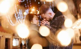 Artificial lighting by garlands. Happy multiracial couple together outdoors in the city celebrating New year photo