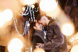 Artificial lighting by garlands. Happy multiracial couple together outdoors in the city celebrating New year photo