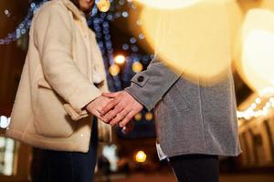 tomándose de las manos. feliz pareja joven celebrando el año nuevo al aire libre en la calle foto