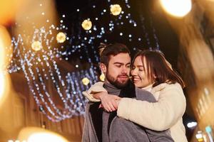 hermosa guirnalda de iluminación. feliz pareja joven celebrando el año nuevo al aire libre en la calle foto