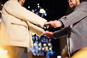 Holding each other by hands. Happy young couple celebrating New year outdoors on the street photo