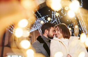 abrazándose unos a otros. feliz pareja joven celebrando el año nuevo al aire libre en la calle foto