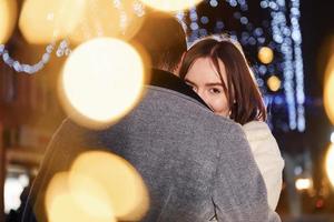 hermosa guirnalda de iluminación. feliz pareja joven celebrando el año nuevo al aire libre en la calle foto