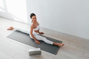 On yoga mat. Young caucasian woman with slim body shape is indoors at daytime photo