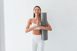 With mat in hands. Young caucasian woman with slim body shape is indoors at daytime photo