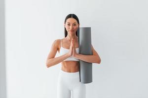 With mat in hands. Young caucasian woman with slim body shape is indoors at daytime photo