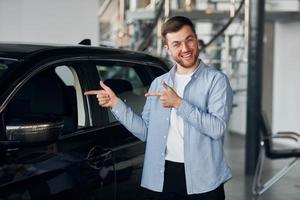 Successful man in glasses standing near brand new car indoors photo