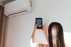 vista trasera de la mujer que está de pie en el interior con el teléfono y controla la tecnología de la casa inteligente foto