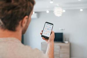 Holds phone. Rear view of adult man that is indoors controlling smart home technology photo