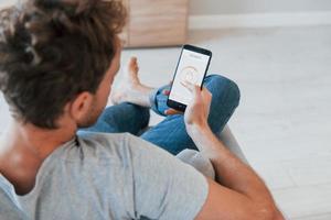 Holds phone. Rear view of adult man that is indoors controlling smart home technology photo