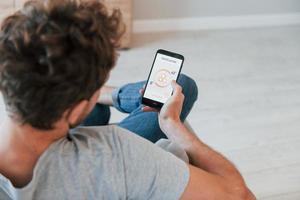 Holds phone. Rear view of adult man that is indoors controlling smart home technology photo