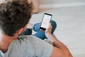 Holds phone. Rear view of adult man that is indoors controlling smart home technology photo