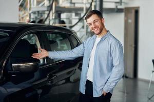 Successful man in glasses standing near brand new car indoors photo