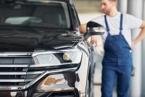 Front view of the car. Young man in white shirt and blue uniform repairs automobile photo