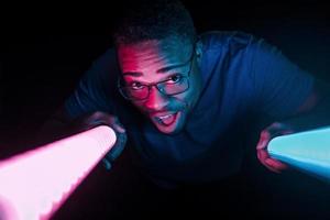 Holds lighting equipment. Futuristic neon lighting. Young african american man in the studio photo