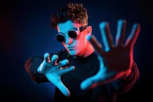 Against black background. Neon lighting. Young european man is in the dark studio photo