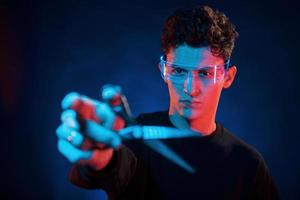 Stylish look. Neon lighting. Young european man is in the dark studio photo