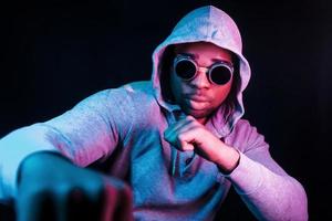 Cyberpunk style glasses. Futuristic neon lighting. Young african american man in the studio photo