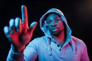 In special eyewear. Futuristic neon lighting. Young african american man in the studio photo