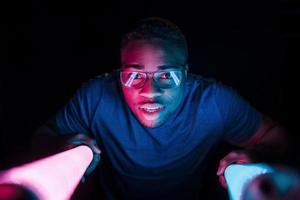 Holds lighting equipment. Futuristic neon lighting. Young african american man in the studio photo