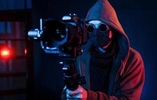 Guy in hood with camera. Neon lighting. Young european man is in the dark studio photo