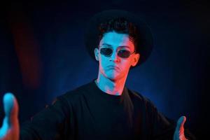 Stylish look. Neon lighting. Young european man is in the dark studio photo