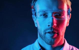 In glasses with display. Neon lighting. Young european man is in the dark studio photo