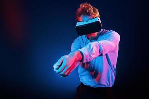 Virtual glasses gaming experience. Neon lighting. Young european man is in the dark studio photo