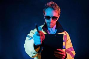 In police uniform. Neon lighting. Young european man is in the dark studio photo