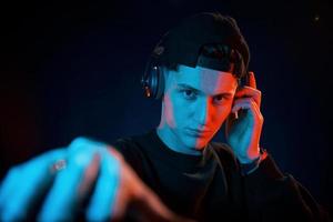 Guy uses headphones. Neon lighting. Young european man is in the dark studio photo