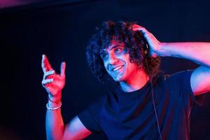 With headphones. Young beautiful man with curly hair is indoors in the studio with neon lighting photo