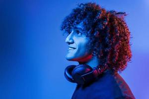 With headphones. Young beautiful man with curly hair is indoors in the studio with neon lighting photo