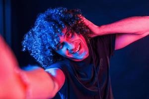 toma autofoto un joven hermoso con el pelo rizado está en el interior del estudio con luces de neón foto