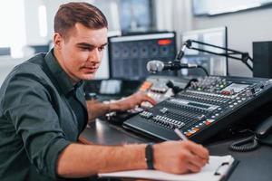 Document with scenario. Young man is indoors in the radio studio is busy by broadcast photo