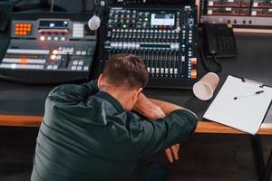 Tired by work. Young man is indoors in the radio studio is busy by broadcast photo