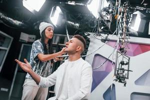 el joven se está preparando para la transmisión de televisión en línea. mujer ayuda a maquillarse foto