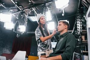 Young man is preparing for TV online broadcast. Woman helps with make up photo