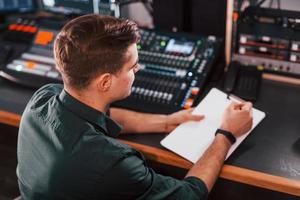 Document with scenario. Young man is indoors in the radio studio is busy by broadcast photo