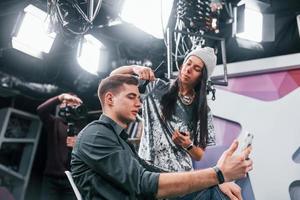 Young man is preparing for TV online broadcast. Woman helps with make up photo