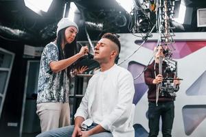 Young man is preparing for TV online broadcast. Woman helps with make up photo