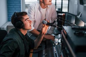 Conception of teamwork. Two guys is indoors in the radio studio is busy by broadcast photo