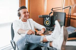 Talks and uses mic. Young man is indoors in the radio studio is busy by broadcast photo