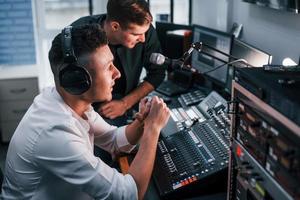 Conception of teamwork. Two guys is indoors in the radio studio is busy by broadcast photo