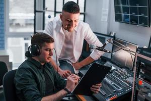 Conception of teamwork. Two guys is indoors in the radio studio is busy by broadcast photo